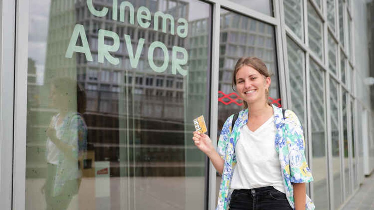 Une femme tient la carte Sortir ! dans sa main devant un cinéma.