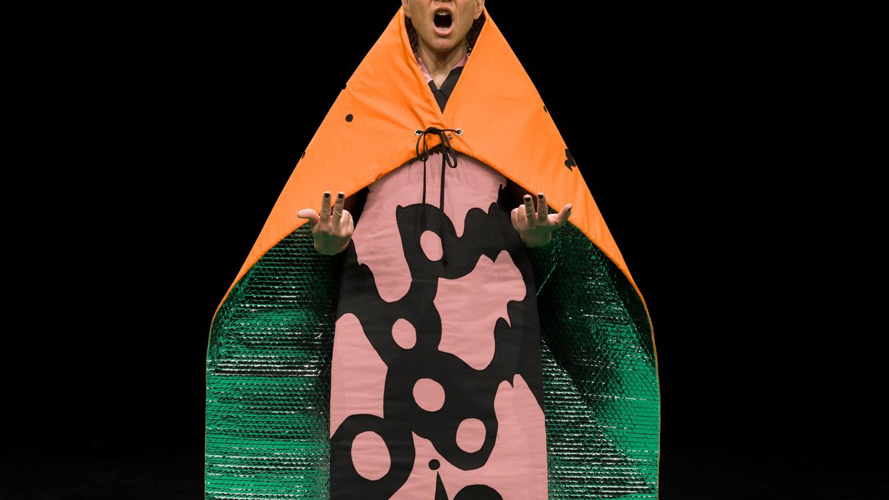 Violaine Lochu chante, elle porte une cape orange sur les épaules.