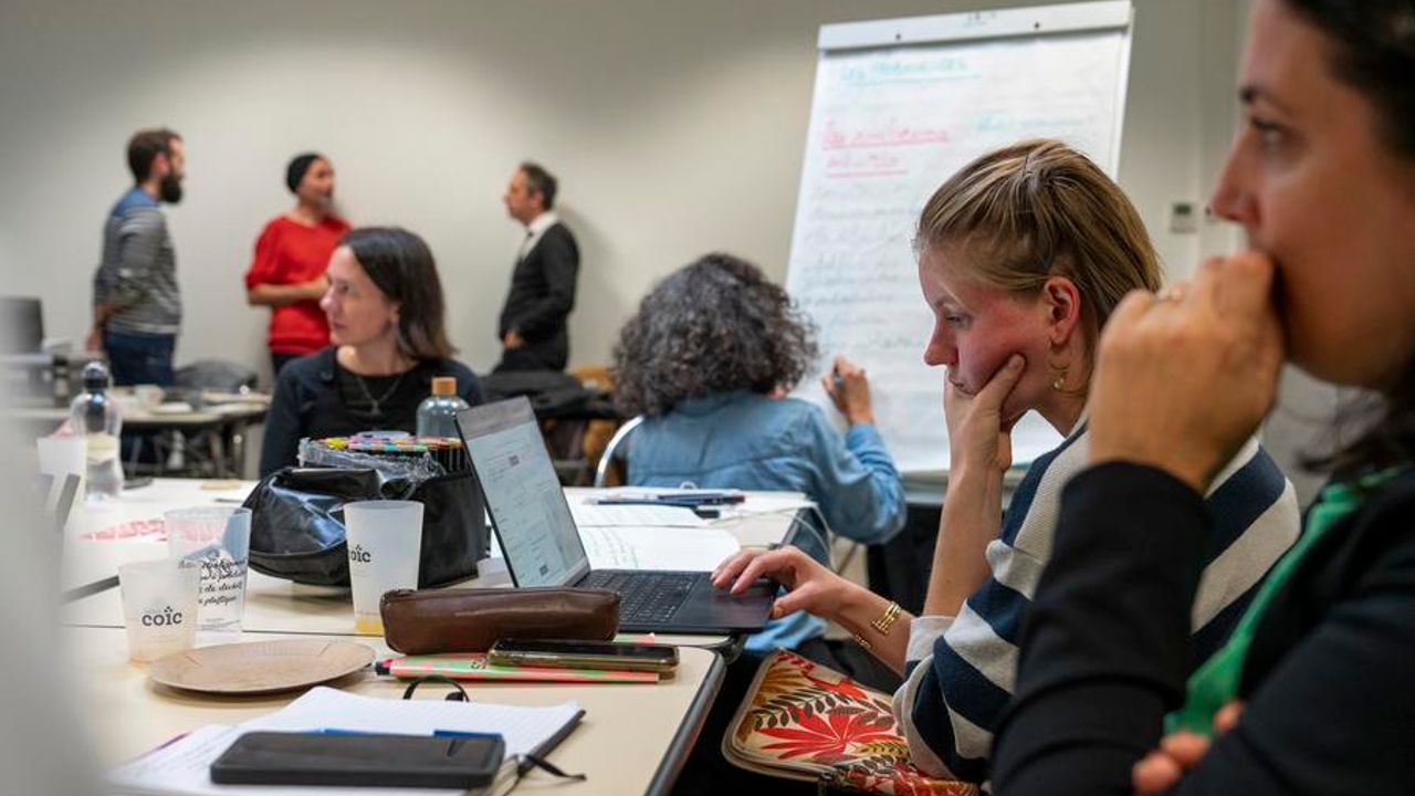 Plusieurs personnes autour d'une table avec des ordinateurs et un tableau blanc.