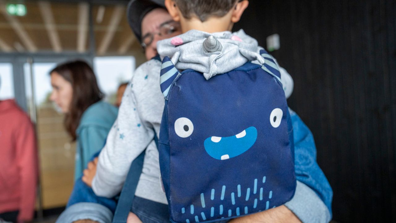 Un jeune enfant dans les bras de son père s’apprête à faire sa rentrée.