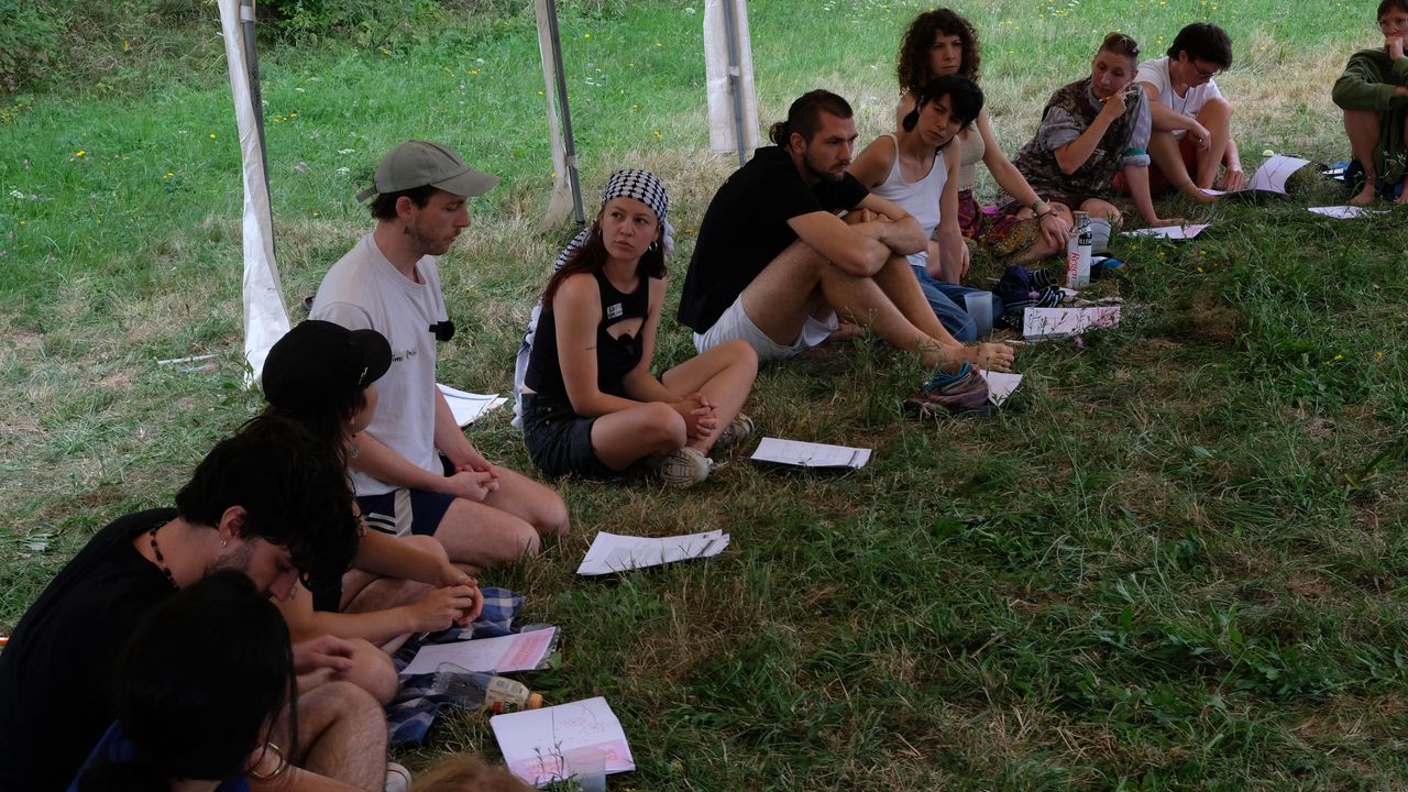 People sitting on the grass at a workshop, with papers in front of them