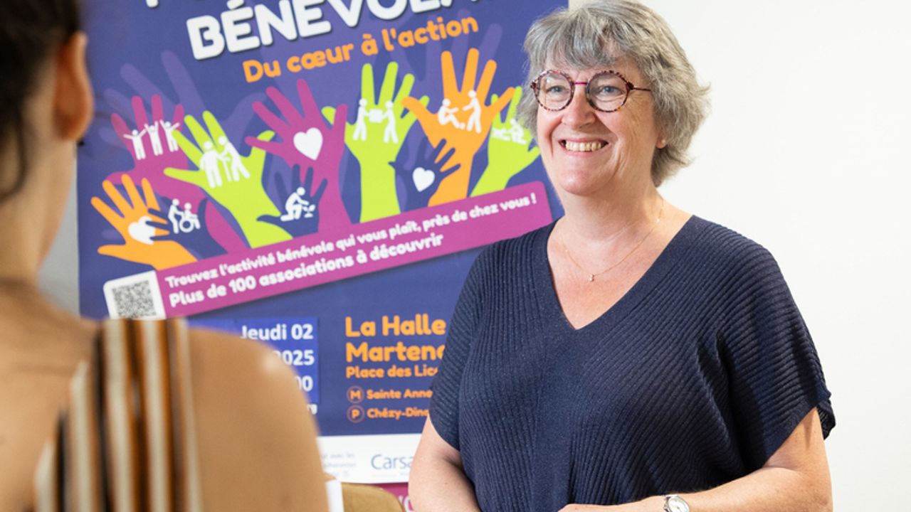 Une femme se tient devant l'affiche du forum France Bénévolat