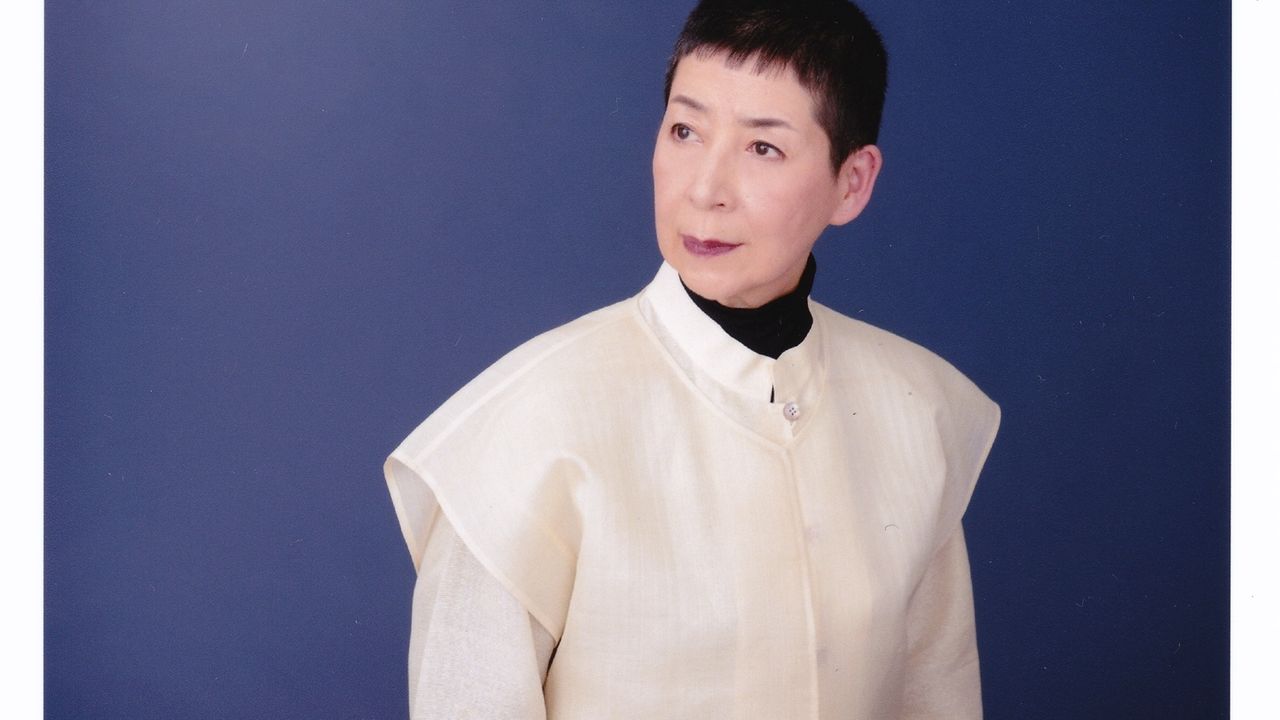 Ambiance zen en perspective avec l'artiste japonaise Midori Takada, vêtue de blanc sur un fond bleu, sur cette photographie.