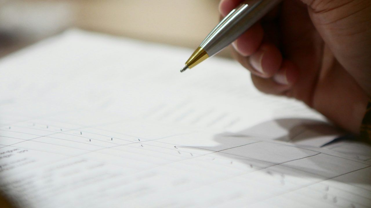 gros plan sur une main qui tient un crayon et va signer un papier