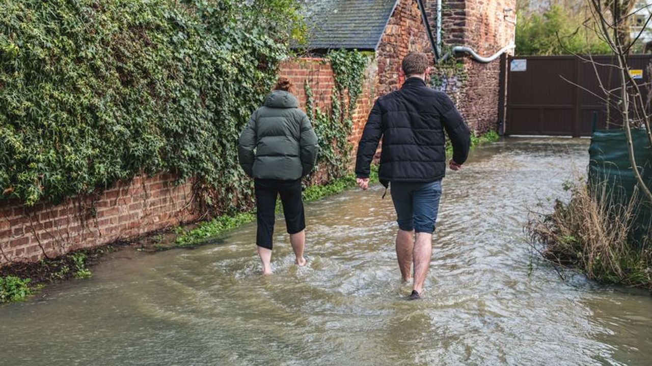 deux personnes marchent dans l'eau devant leur domicile