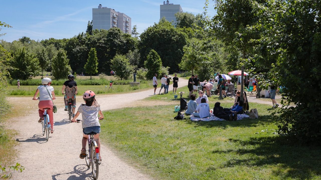 Au coeur des prairies Saint-Martin, avec des cyclistes au premier plan, et des gens se reposant à l'ombre sur la pelouse, à droite. En arrière-plan, des immeubles