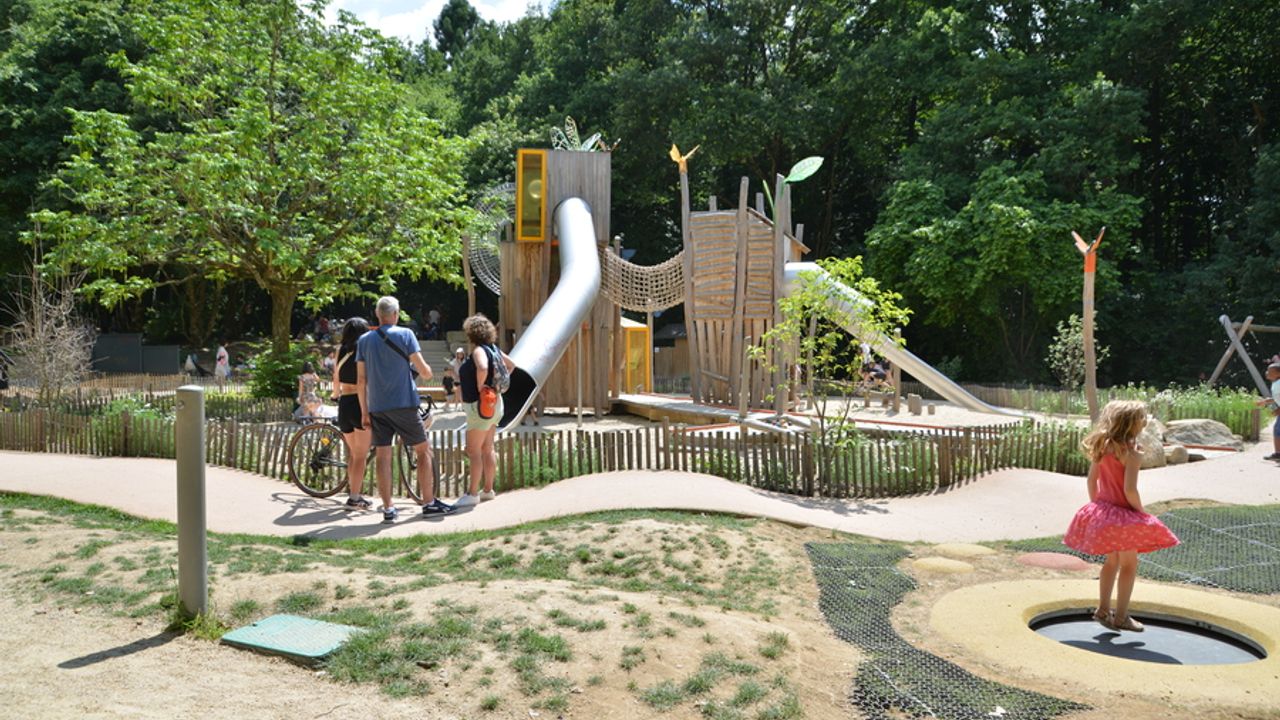 Des jeux pour enfants en plein air, avec une jeune fille rebondissant sur un trempoline au premier plan et un tobogan au second plan