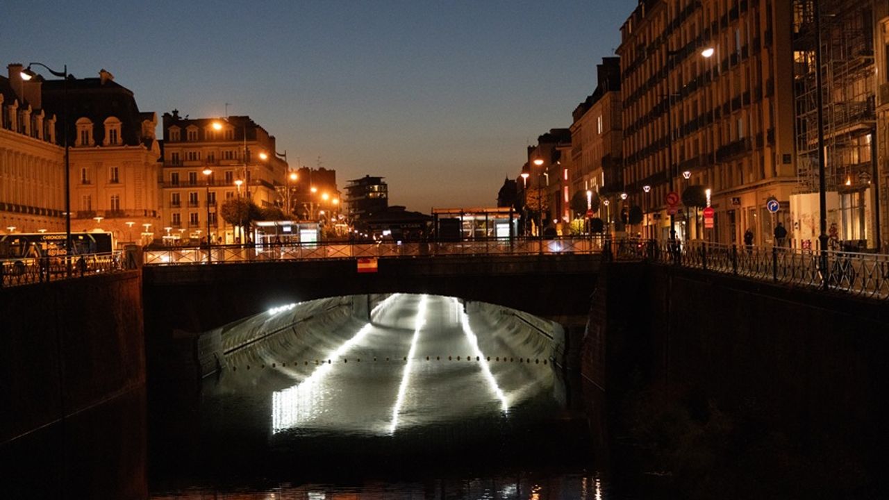 Vue au crépuscule, prise mi-octobre 2025, des quais, avec la Vilaine au premier plan, puis la dalle à partir de République au milieu de l'image, avec, en dessous, un éclairage blanc par des projecteurs éclairant le dessous des dalles et se reflétant sur la Vilaine.