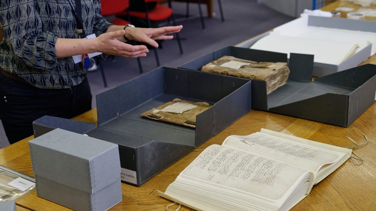 Femme présentant des boîtes d’archives contenant des documents anciens.