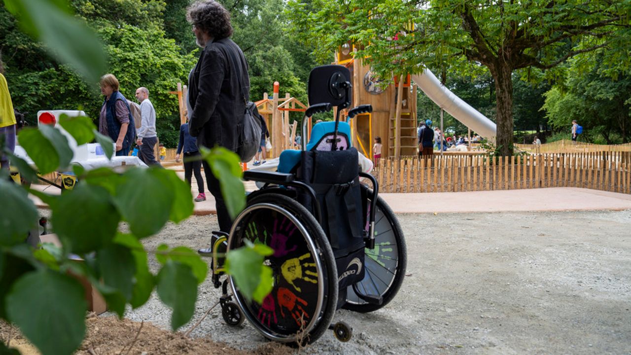 Un enfant dans un fauteuil roulant devant une aire de jeux adaptée.