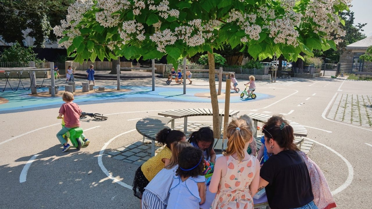 Des enfants jouent dans une cour de récréation végétalisée.