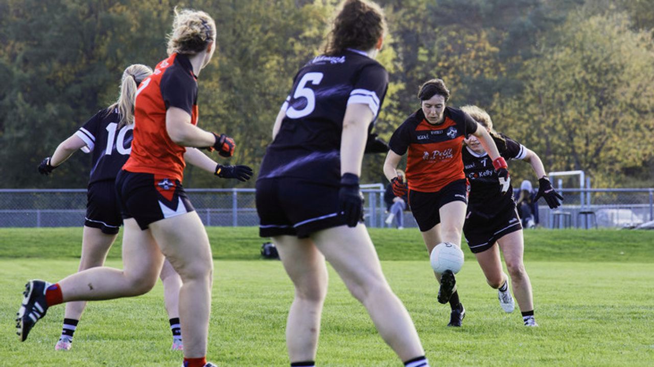 Des joueuses en noir de Londres et d'autres en rouge et noir de Rennes, se disputent une balle ronde dans un match de football gaélique. 