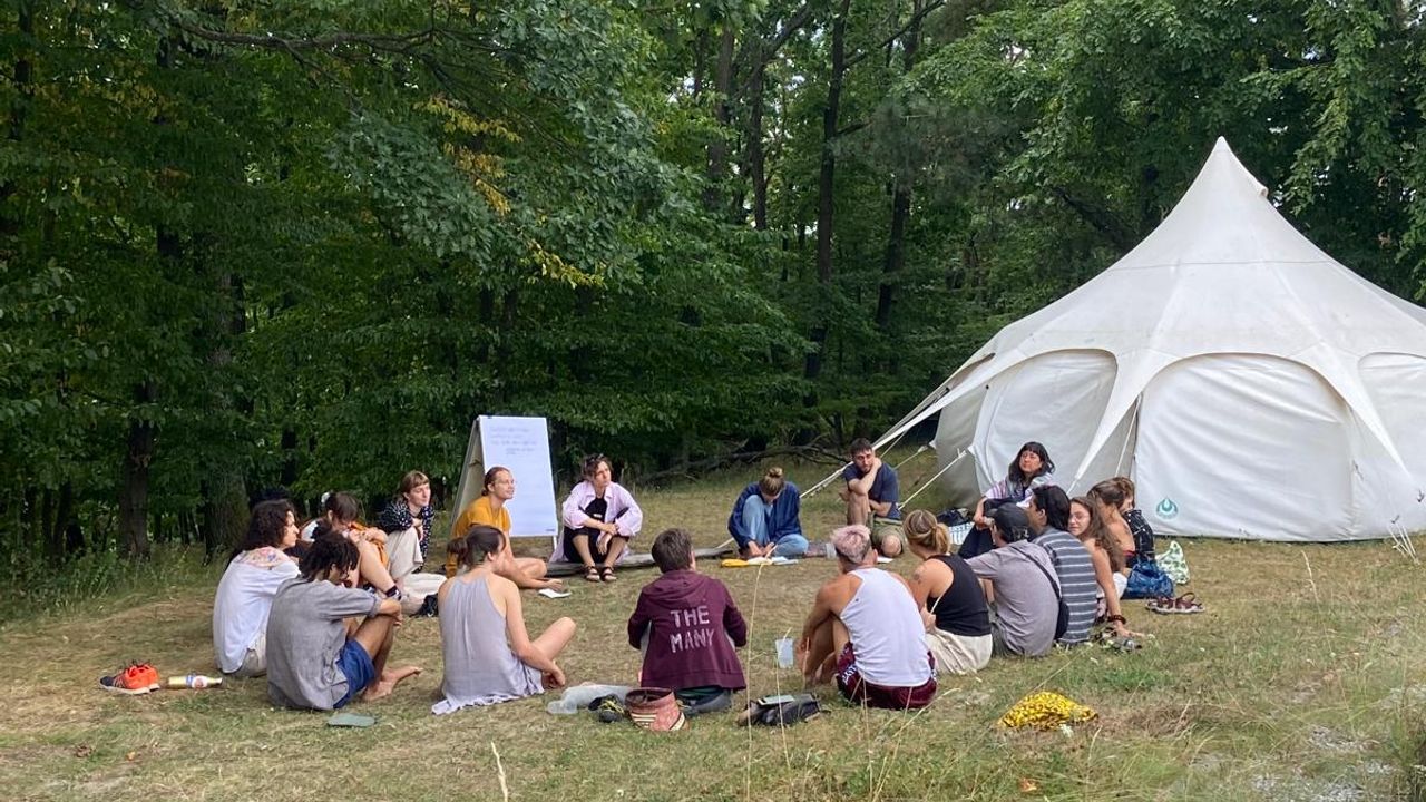 people sitting on the grass in a circle next to a tent at a workshop