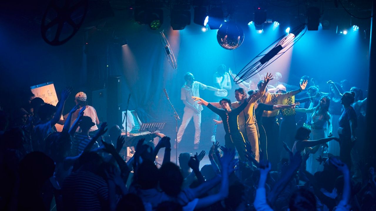 Vue d'une salle de spectacle. L'éclairage est bleu. Les spectateurs lèvent les bras en l'air, comme les gens sur scène. Vous vous trouvez au Marathon de la danse du festival Waterproof.