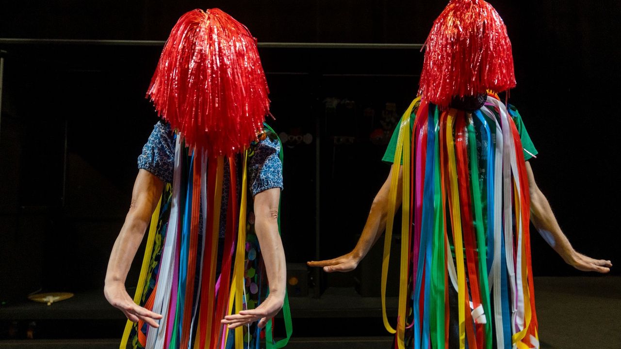 Une actrice et un acteur en costume avec rideaux colorés et Pompons sur la tête
