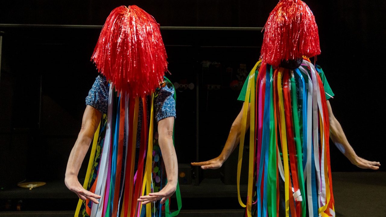 Une actrice et un acteur en costume avec rideaux colorés et Pompons sur la tête