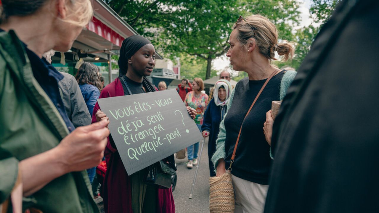 Une femme tient une pancarte posant la question suivante : « Vous êtes-vous déjà senti étranger quelque part ? »