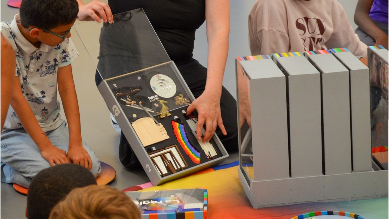 La médiatrice Amandine Braud présente aux enfants les oeuvres miniature du jeu de plateau collaboratif Rejouer La Criée aux enfants. Elles sont de différentes formes et couleurs, et sont inspirées de 40 oeuvres produites par La Criée depuis 40 ans.