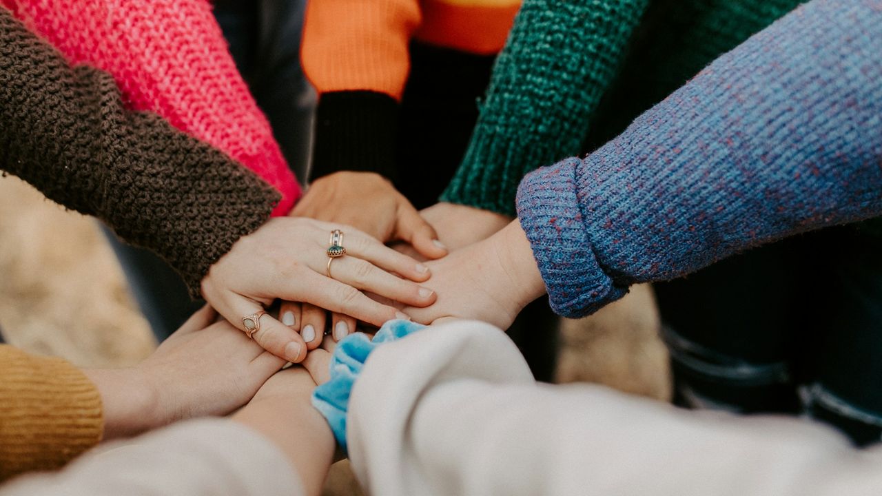 Several people stack their hands together in a circle, showing unity.