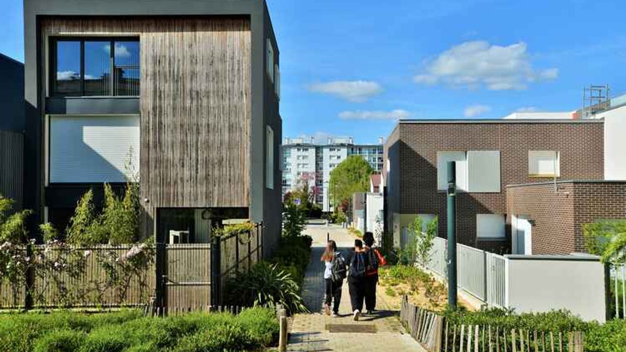 Une voie piétonne entre deux maisons individuelles récentes avec petits jardins. Trois enfants de dos marchent sur cette voie qui est la promenade Odette du Puiguaudeau dans le quartier de Maurepas à Rennes.
