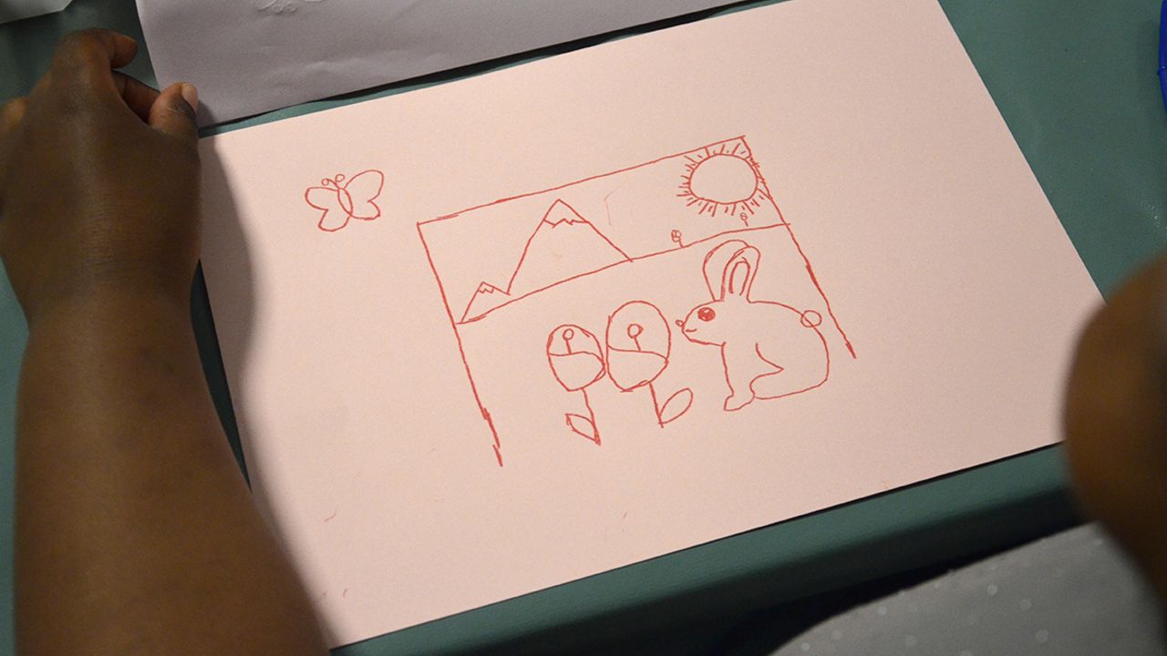 Une élève découvre son dessin devenu rouge sur fond rose après le transfert de la feuille carbone.