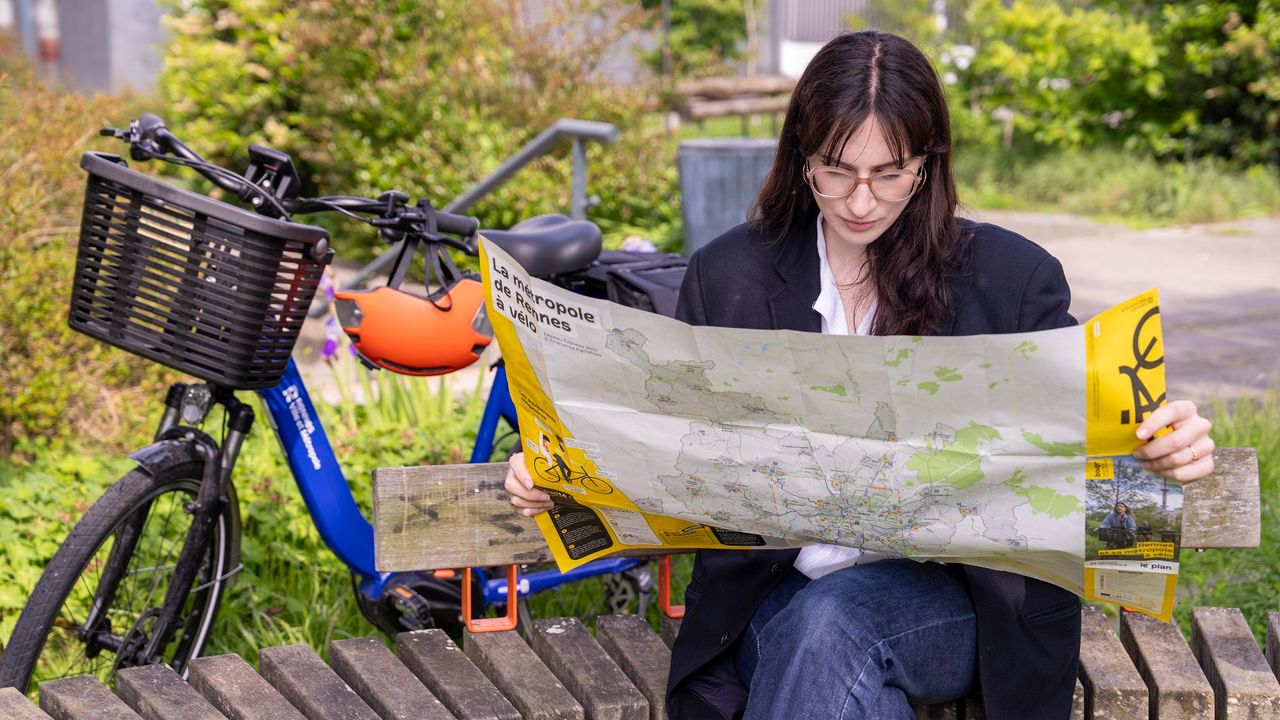 Jeune fille assise consulte une carte d'itinéraires vélo, en arrière plan un VéloSTAR.