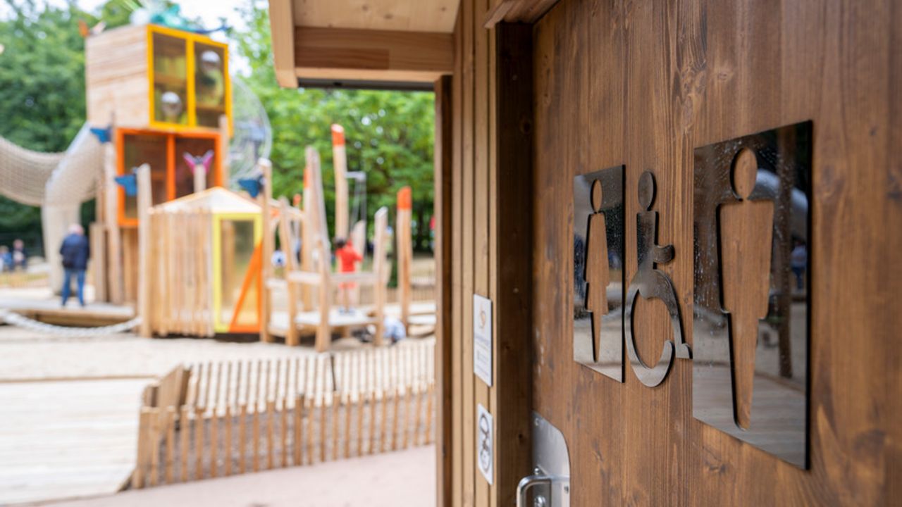 Au premier plan, des WC adaptés. Au second plan, une structure ludique en bois.