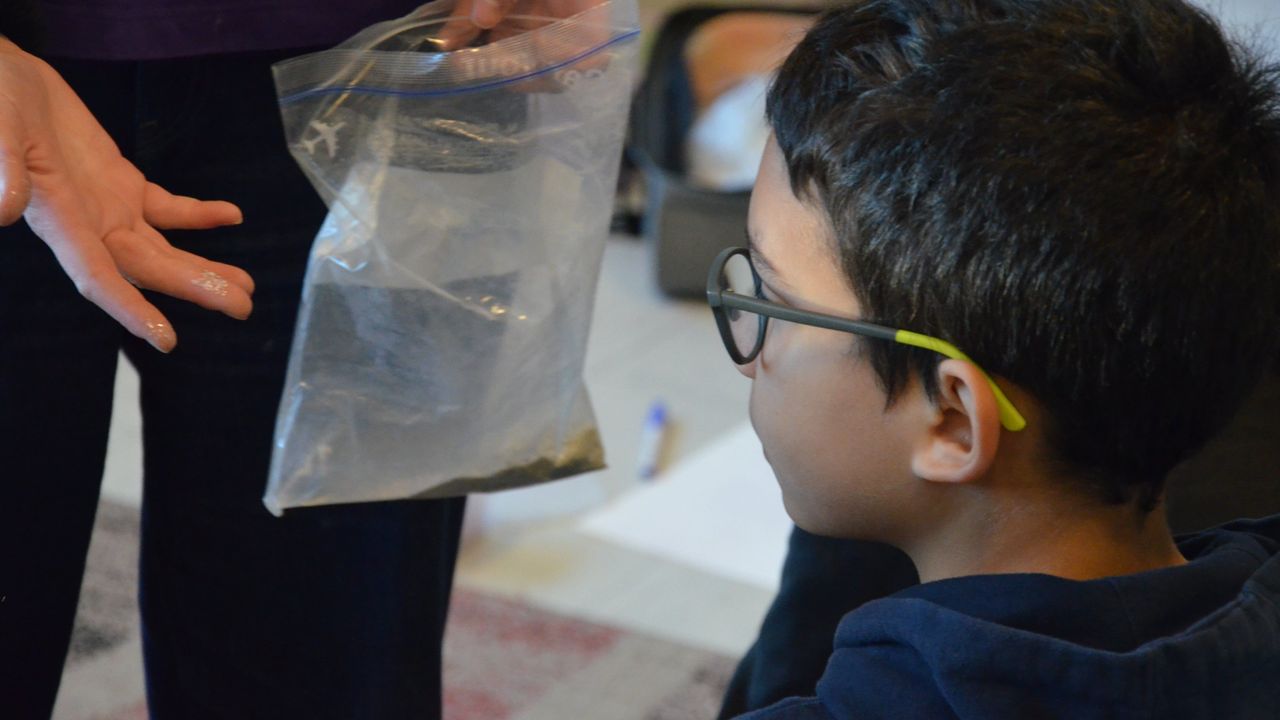Margaux Janisset montre du mica, paillettes de sable à un enfant.