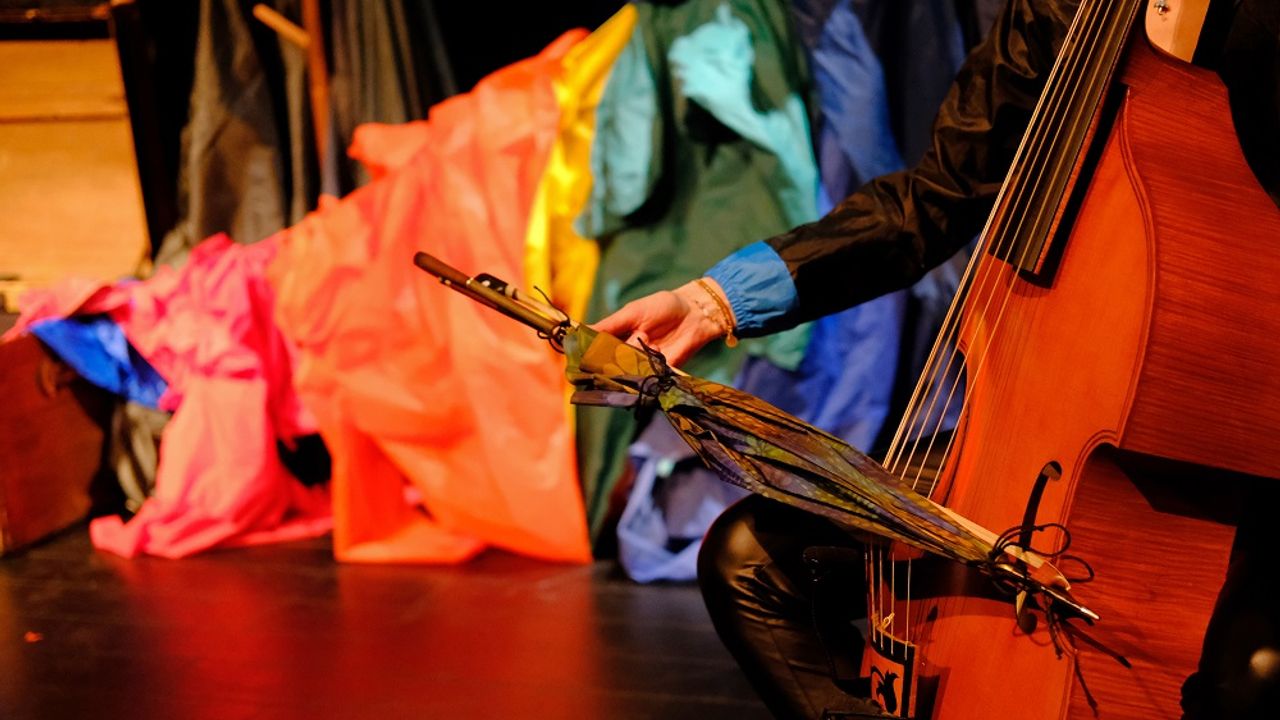 Au 1er plan, quelqu'un joue du violoncelle avec un parapluie.