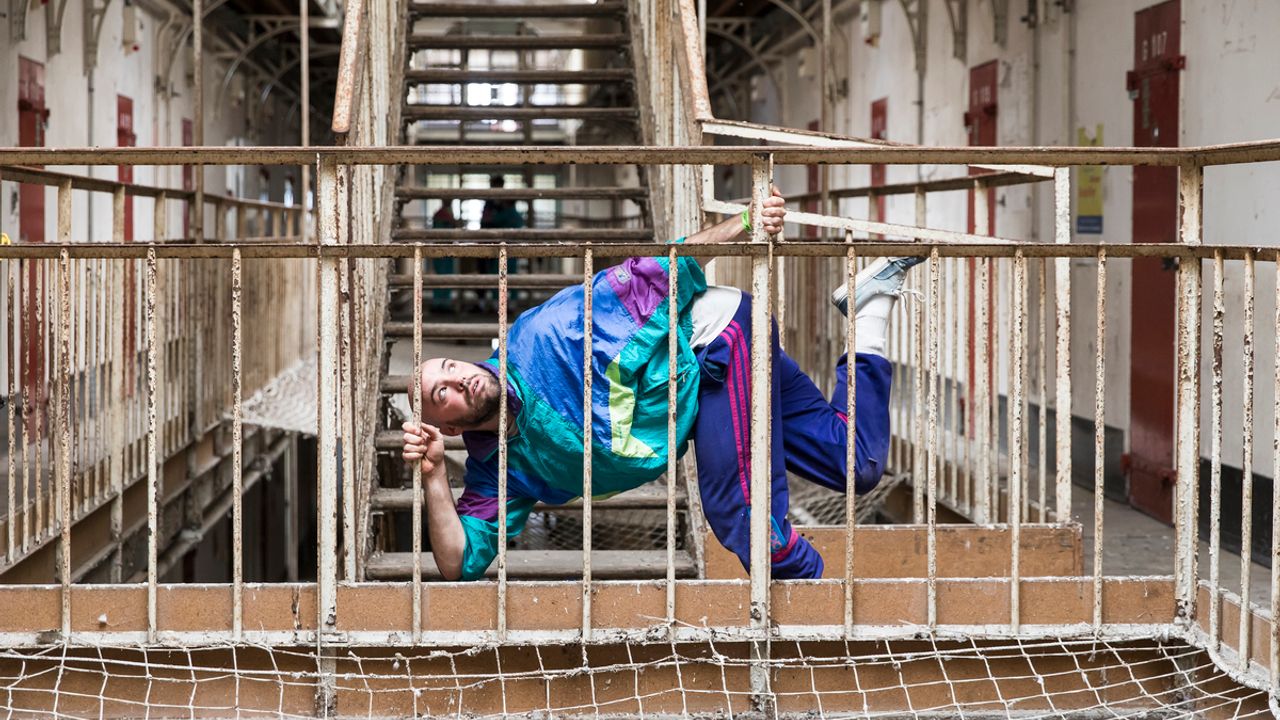 Homme habillé en jogging coloré danse sur une rambarde intérieure de la prison