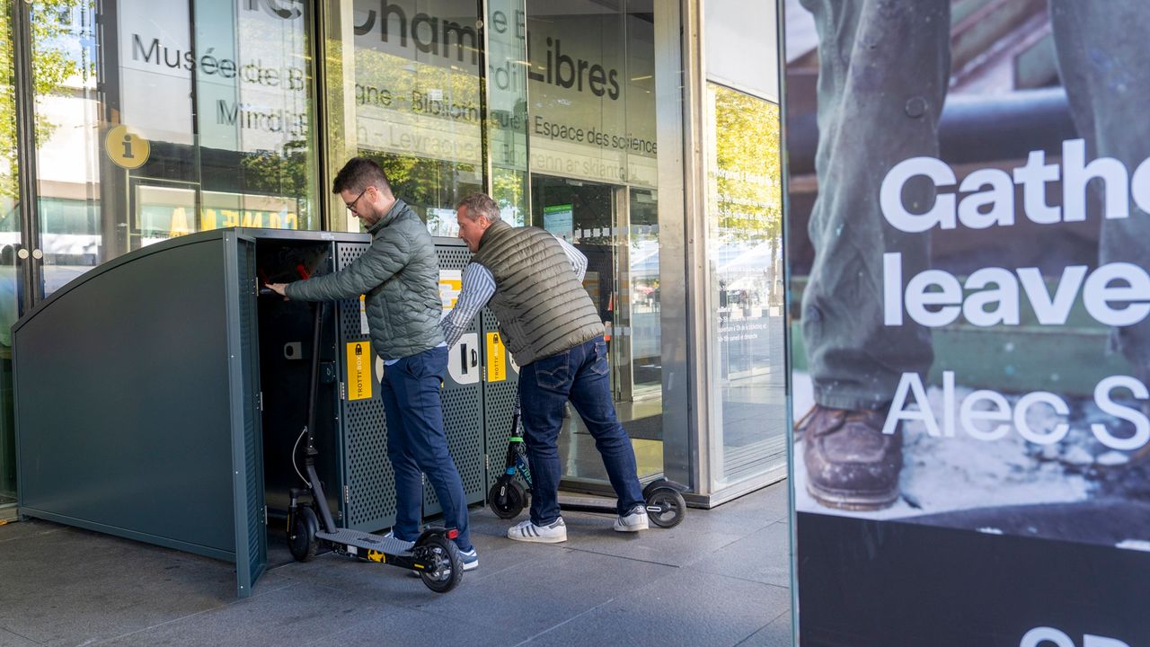 Deux personnes sont en train de stationner des trottinettes dans les box sécurisés.