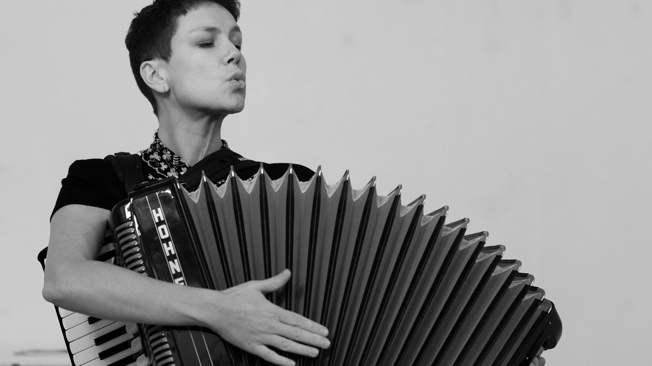 Image en noir et blanc sur laquelle on voit Violaine Lochu tenir un accordéon ouvert. Son visage indique qu'elle est en train de siffler.