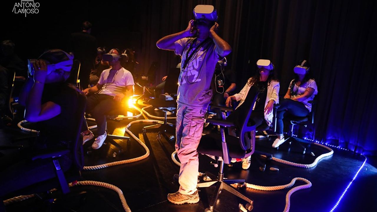 Dans la pénombre, des gens observe quelque chose (un spectacle d'acrobatie) à travers un casque de réalité augmentée.