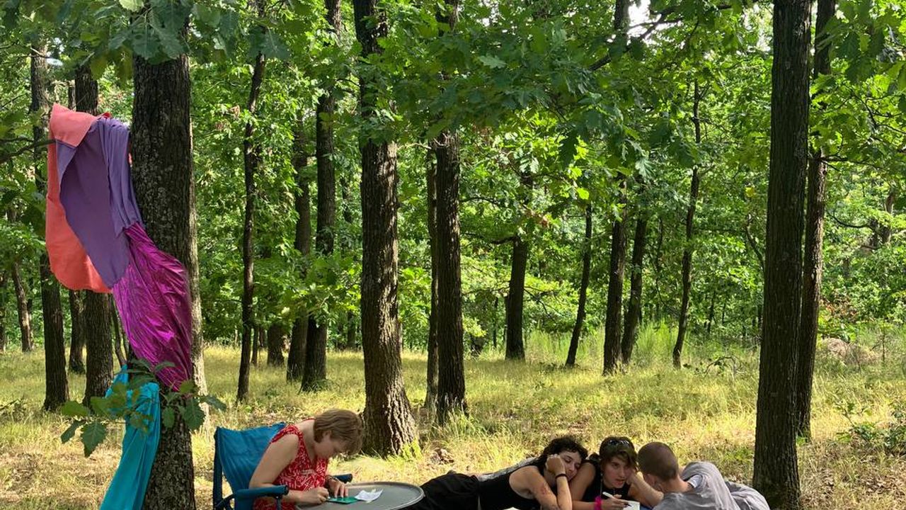 People sitting and lying in the forest ground, reading to each other out loud