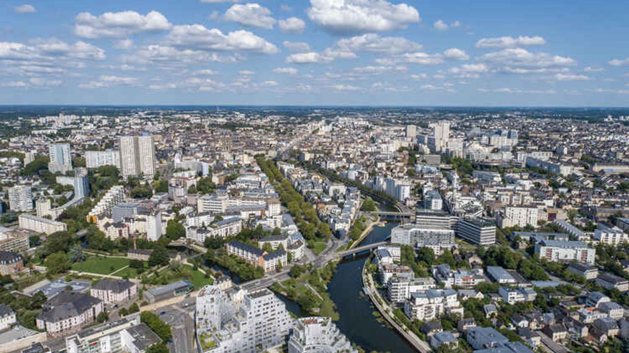 Vue aérienne à l'ouest du centre-ville de Rennes, au-dessus de la Vilaine près du secteur de la Confluence. Au second plan, est visible une grande partie de la ville de Rennes.