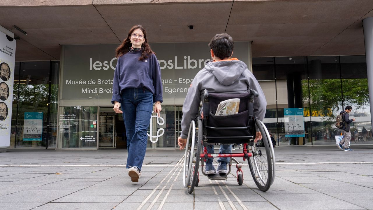 Photo de personnes valide et en fauteuil roulant qui se croisent devant les Champs libres.
