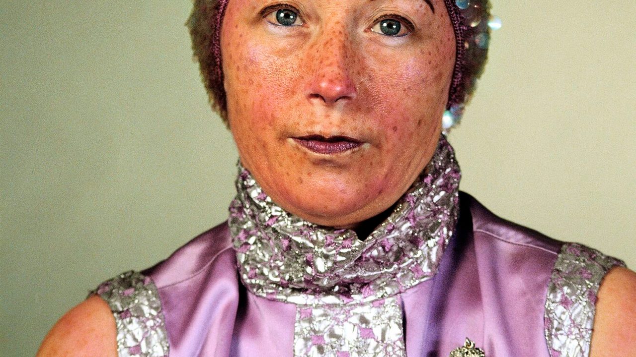 Portrait photographique d'une femme portant un chemisier violet en satin. Un bonnet à sequins sur la tête, des tâches de rousseur, elle regarde droit devant elle