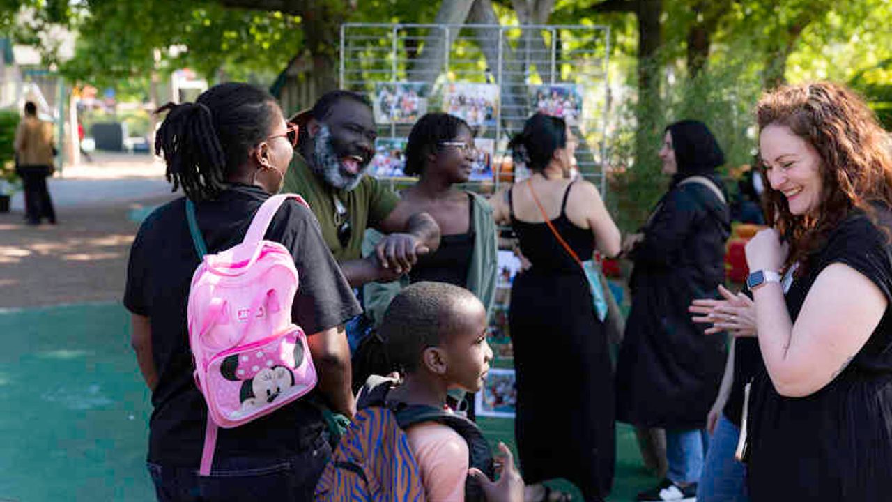 Une famille échange avec l'enseignante du dispositif sur la droite. À l'arrière plan, des invités discutent devant les panneaux créés pour l'occasion.