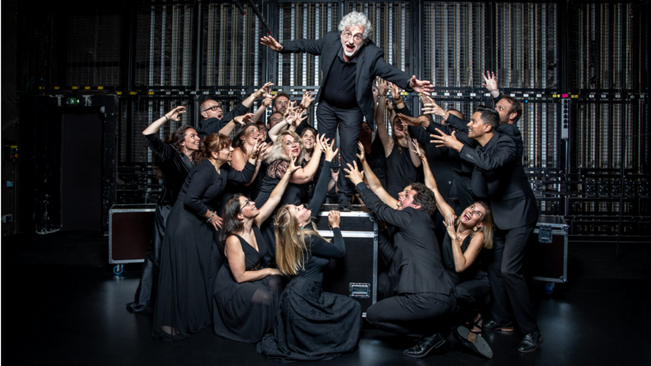 Sur la scène d'une salle de concert, un homme porté par une foule en noir, fait semblant de se jeter dans le vide.