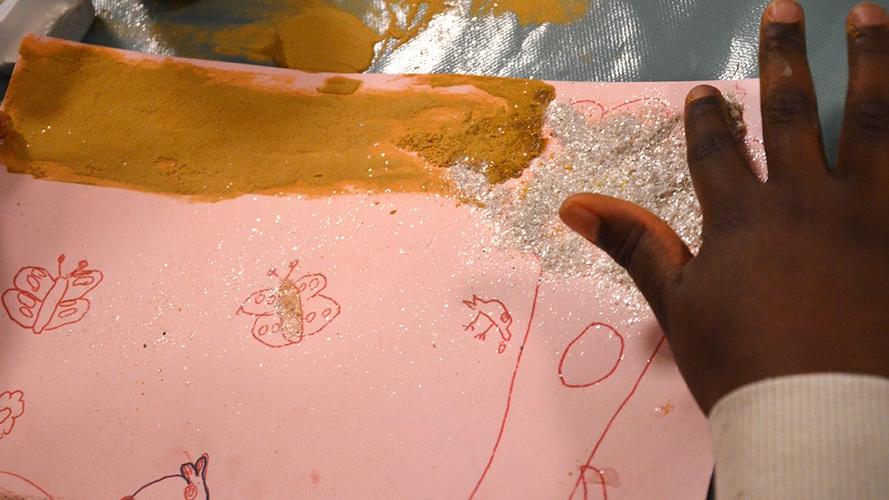 une enfant dépose les paillettes sur son dessin.