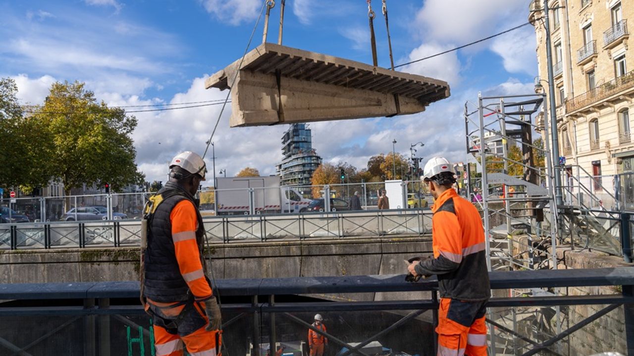 Près du pont de la mission à Rennes, un morceau de gravas, supporté par des cables, au dessus de deux barges sur la Vilaine. Au premier plan, deux ouvriers du chantier de dos,