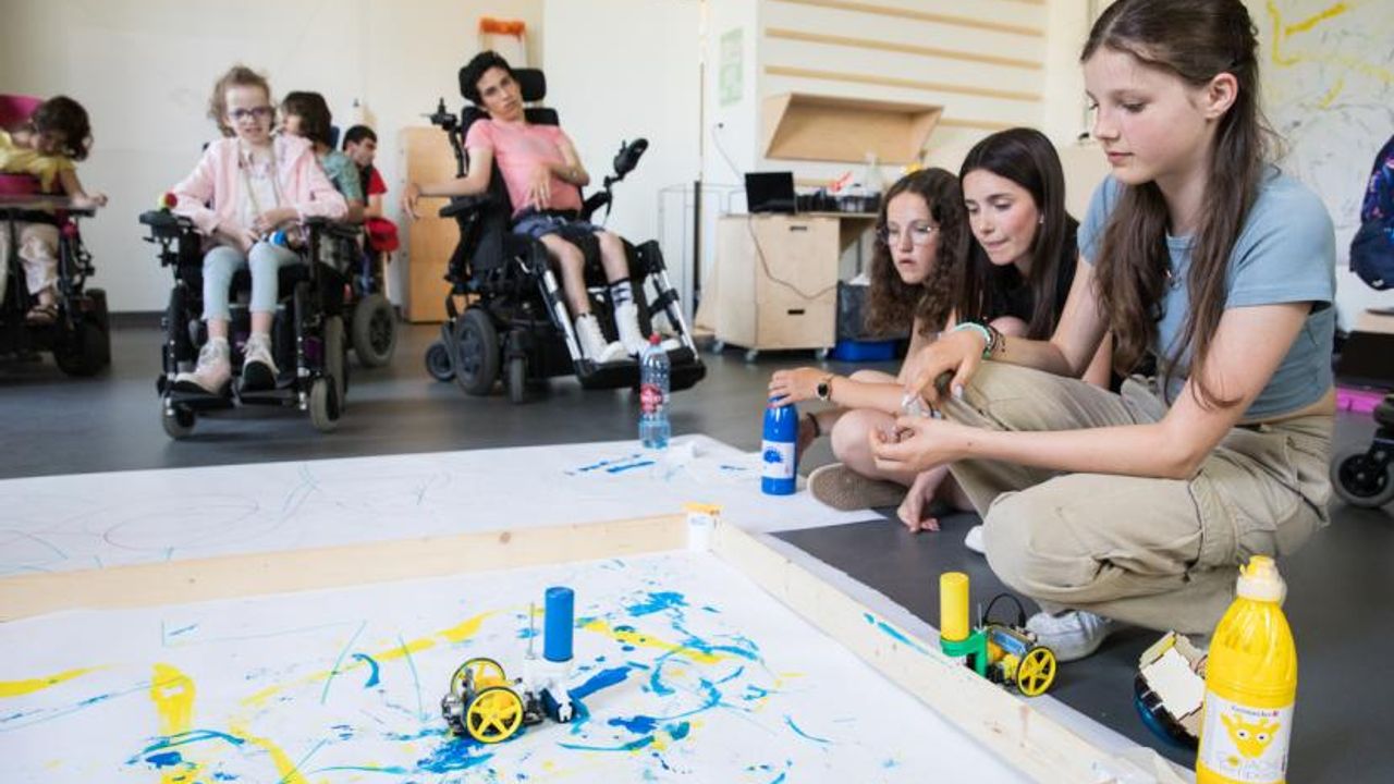 Des collègiens observent un robot en train de peindre avec des jeunes en fauteils roulants.