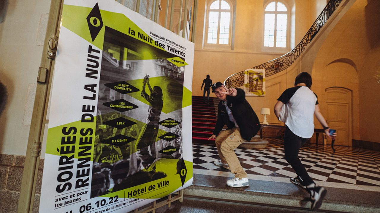 Des jeunes s’amusent dans le hall de l’hôtel de ville de Rennes autour d’une affiche « Soirées Rennes de la nuit ».