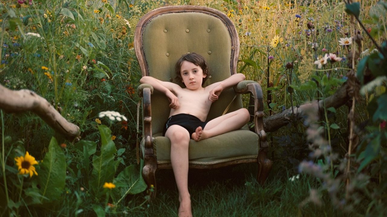 Un enfant en maillot de bain assis dans un fauteuil, dans un jardin luxuriant