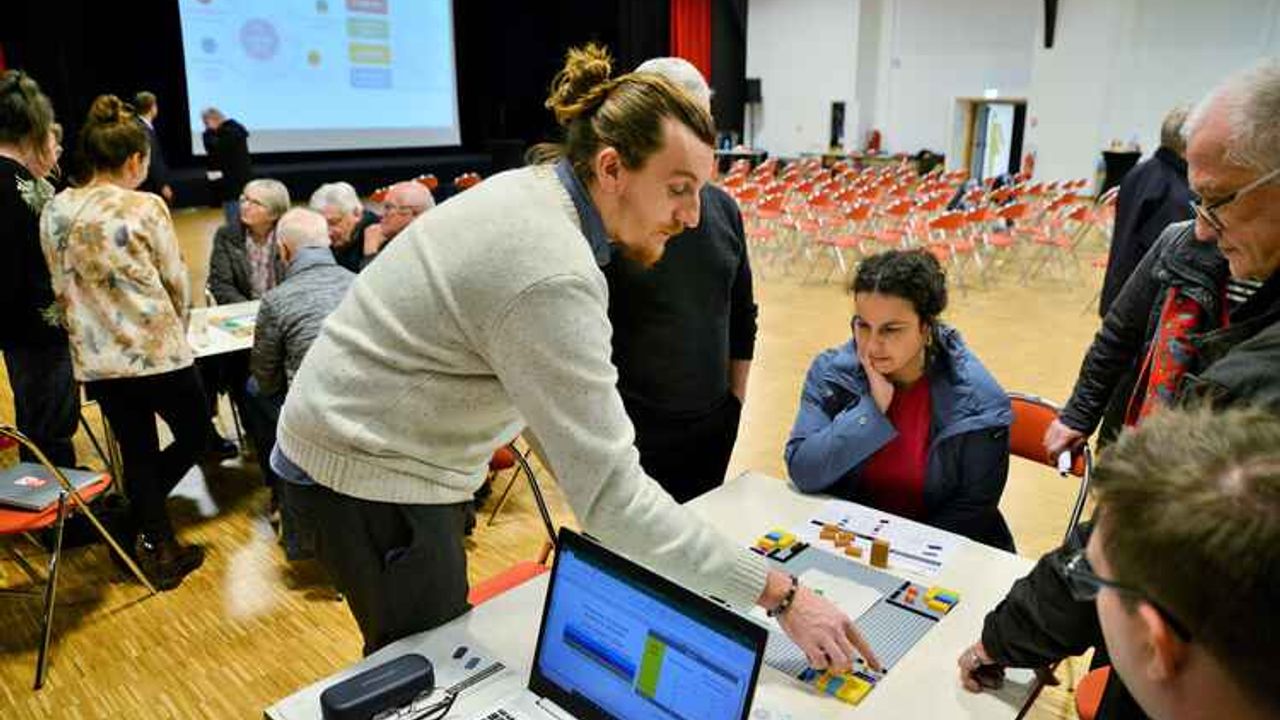 Echanges au premier plan entre personnes autour d'une maquette en lego, sur la gauche au second plan, un autre groupe de personnes échangent autour d'une table. La scène se passe à la salle de la Confluence à Betton en février 2024 lors d'une réunion de concertation concernant le Plan local d'urbanisme intercommunal.