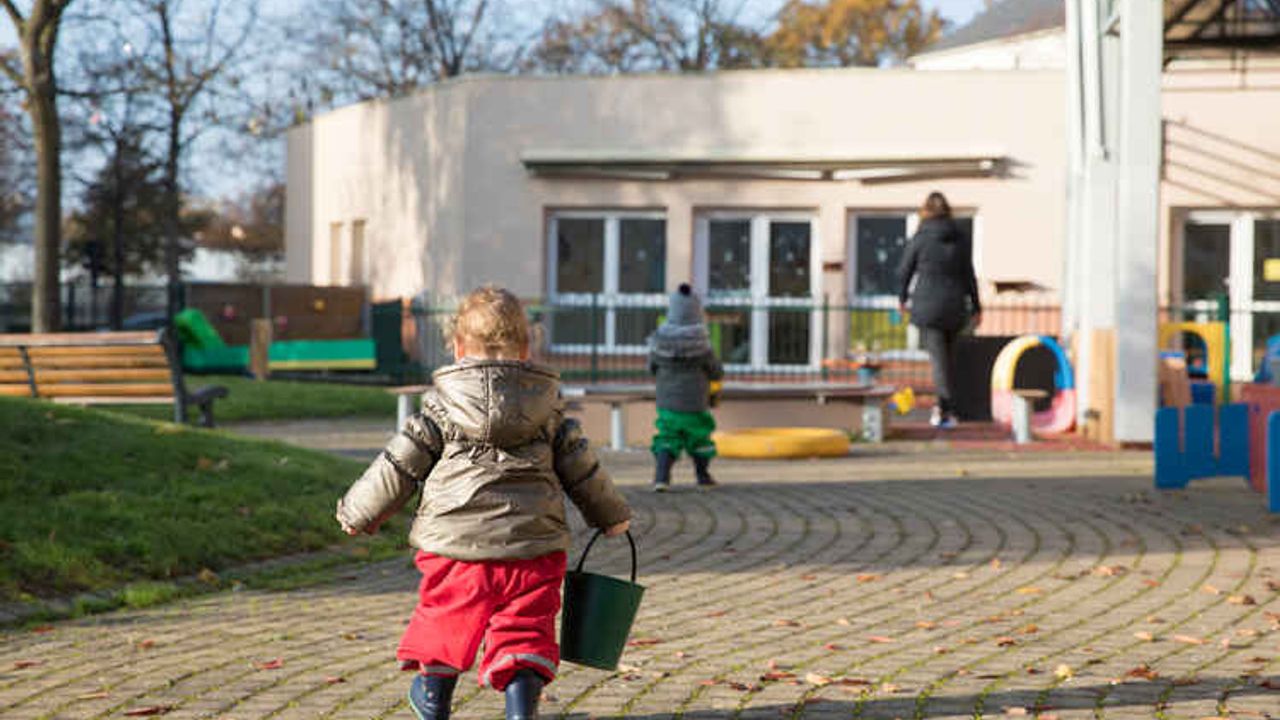Une enfant marche dans la cour de la crèche, un seau à la main