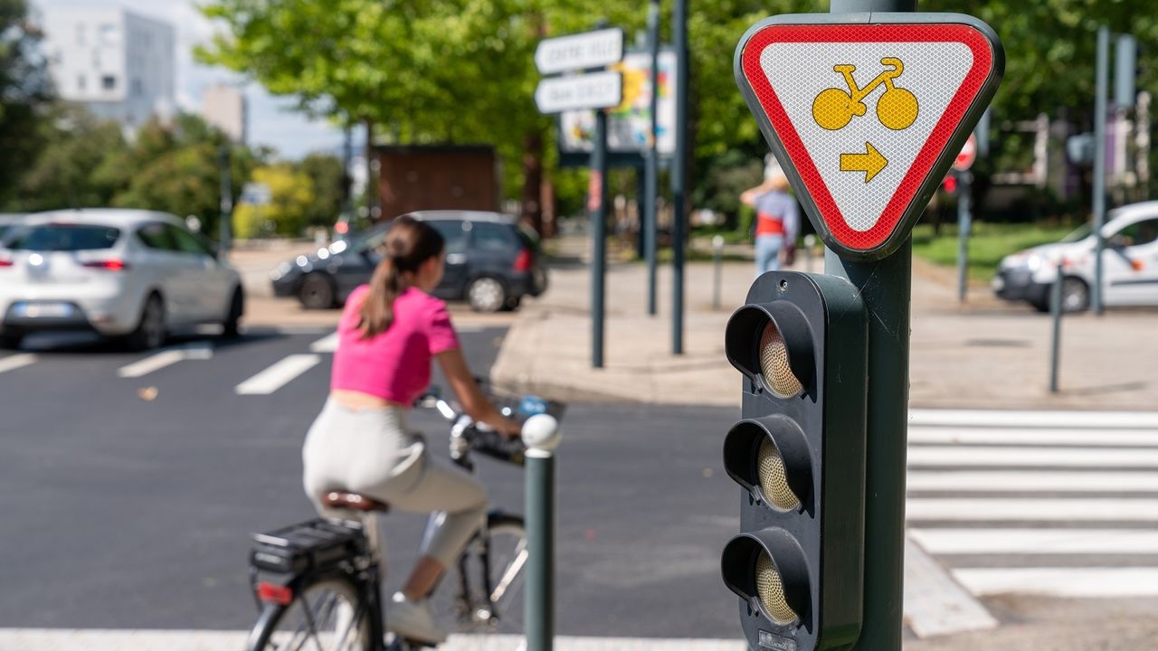 Photo d’une cycliste qui tourne à droite à un carrefour. Un feu tricolore en premier plan.