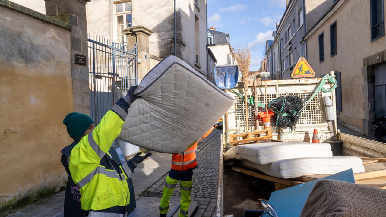 Des agents municipaux enlèvent un matelas de la rue pour le mettre dans un camion.