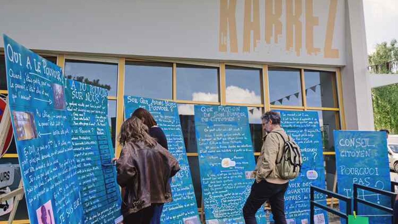 Des personnes lisent des affiches sur le thème "Conseil citoyen : pourquoi pas toi ?"