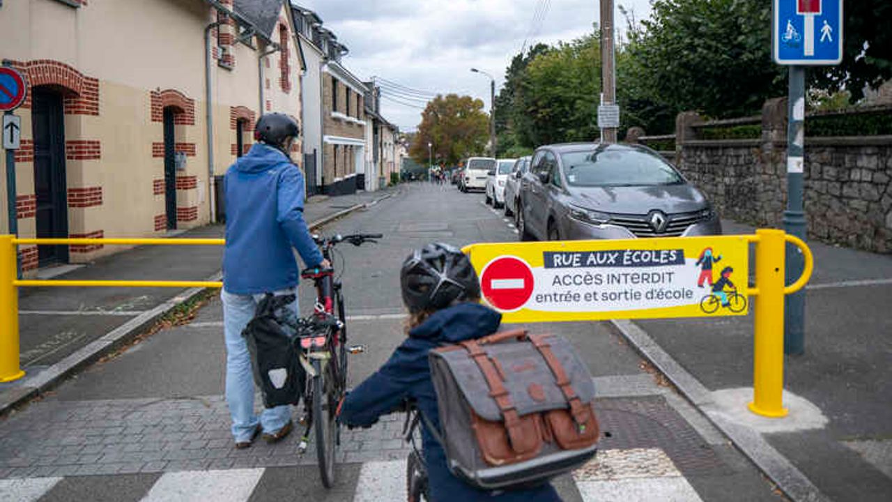 un adulte et un enfant passent la barrière installée pour empêcher le passage des voitures dans la rue de l'école. 